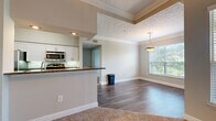 Located at 6850 Peachtree Dunwoody Rd in Sandy Springs, GA, this single-floor residence offers a well-designed, open-concept layout that seamlessly connects the kitchen, dining, and living areas. The kitchen is a standout feature, equipped with stainless steel appliances including a microwave and range, crisp white cabinetry, dark granite countertops, and a peninsula with a built-in sink — ideal for both cooking and casual dining. The living and dining areas are defined by rich hardwood-style flooring, elegant crown molding, and a decorative ceiling detail that adds architectural interest. A pendant light fixture anchors the dining space, while large windows fitted with blinds invite an abundance of natural light and offer views of surrounding greenery. Carpeted bedrooms provide a comfortable retreat, each featuring ceiling fans, generous wall space, and windows that frame leafy outdoor views. The primary bathroom is well-appointed with a dual-sink vanity, white cabinetry, a wide mirror, and a glass-enclosed shower. Additional highlights include a spacious walk-in closet with wire shelving and recessed lighting throughout, contributing to a bright and functional living environment.