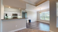 Located at 6850 Peachtree Dunwoody Rd in Sandy Springs, GA, this single-floor residence offers a well-designed, open-concept layout that seamlessly connects the kitchen, dining, and living areas. The kitchen is a standout feature, equipped with stainless steel appliances including a microwave and range, crisp white cabinetry, dark granite countertops, and a peninsula with a built-in sink — ideal for both cooking and casual dining. The living and dining areas are defined by rich hardwood-style flooring, elegant crown molding, and a decorative ceiling detail that adds architectural interest. A pendant light fixture anchors the dining space, while large windows fitted with blinds invite an abundance of natural light and offer views of surrounding greenery. Carpeted bedrooms provide a comfortable retreat, each featuring ceiling fans, generous wall space, and windows that frame leafy outdoor views. The primary bathroom is well-appointed with a dual-sink vanity, white cabinetry, a wide mirror, and a glass-enclosed shower. Additional highlights include a spacious walk-in closet with wire shelving and recessed lighting throughout, contributing to a bright and functional living environment.