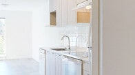 Located at 1408 E 15th Ave in Vancouver's Kensington-Cedar Cottage neighbourhood, this well-appointed one-bedroom, one-bathroom unit offers a clean, modern aesthetic defined by light tones and warm wood-look flooring throughout. The entrance leads into a thoughtfully designed open-concept space where the kitchen, dining, and living areas flow together seamlessly. The kitchen is efficiently laid out with light wood cabinetry, white subway tile backsplash, white appliances including a range, dishwasher, and refrigerator, and generous counter space. Track lighting overhead keeps the kitchen area bright and functional. The living area is bathed in natural light, enhanced by a sliding glass door that opens directly onto a private balcony with pleasant treetop and neighbourhood views. The bedroom offers a comfortable footprint with a built-in closet featuring full-length panel doors, clean white walls, and warm flooring. Additional storage is provided by multiple closets throughout the unit. The bathroom is finished in a crisp white palette, complete with a soaker tub and shower combination, tiled surround, vanity with integrated sink, and chrome fixtures. In-unit laundry adds everyday convenience. The space presents a bright, minimalist character well-suited to efficient urban living.