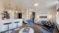 This single-floor studio unit showcases a thoughtfully designed open-concept layout that seamlessly integrates the living, sleeping, and kitchen areas into one cohesive space. Dark hardwood-style flooring runs throughout, grounding the bright white walls and creating a modern, urban aesthetic.

The kitchen is efficiently arranged in an L-shape, featuring white flat-front cabinetry, a white quartz countertop, an induction cooktop, stainless steel sink, dishwasher, and a wall-mounted utensil rail. Open dark shelving adds functional display space, while glass pendant lights above the breakfast bar lend a decorative touch. A wall-mounted mini-split HVAC unit ensures year-round climate control.

The living area benefits from large arched and rectangular windows that flood the space with natural light and offer views of the surrounding streetscape. A built-in open shelving unit provides additional storage and organization near the entryway.

A sliding black barn door leads to the bathroom, which features a subway-tiled walk-in shower, a pedestal sink, concrete-style flooring, and open built-in shelving for toiletries and linens. The sleeping area is integrated into the main living space, completing this compact yet well-appointed studio.
