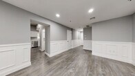 Located at 223 Meadow St in Naugatuck, CT, this two-story home offers three bedrooms, two bathrooms, and a well-planned layout spread across two floors. The main level features a spacious living room distinguished by elegant white wainscoting panels, recessed lighting, and durable wood-look flooring in a warm gray tone that flows throughout the home. The kitchen is efficiently designed in a galley style, equipped with white shaker cabinetry, stainless steel appliances including a range, microwave, and refrigerator, and light stone-look countertops. Both bathrooms are finished with clean white vanities and walk-in shower stalls, complemented by the same wood-look flooring for a cohesive aesthetic. The three bedrooms are bright and neutral, with gray walls, white trim, and windows that invite natural light. The generously sized primary bedroom provides ample space for comfortable living. Additional features include six closets offering abundant storage, a dedicated laundry area, and two staircases connecting the floors. The lower level also benefits from recessed lighting and wainscoting detail, maintaining a consistent, polished look throughout. The home presents a clean, modern interior with a neutral palette well-suited for a variety of living arrangements.