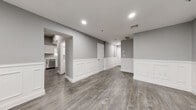 Located at 223 Meadow St in Naugatuck, CT, this two-story home offers three bedrooms, two bathrooms, and a well-planned layout spread across two floors. The main level features a spacious living room distinguished by elegant white wainscoting panels, recessed lighting, and durable wood-look flooring in a warm gray tone that flows throughout the home. The kitchen is efficiently designed in a galley style, equipped with white shaker cabinetry, stainless steel appliances including a range, microwave, and refrigerator, and light stone-look countertops. Both bathrooms are finished with clean white vanities and walk-in shower stalls, complemented by the same wood-look flooring for a cohesive aesthetic. The three bedrooms are bright and neutral, with gray walls, white trim, and windows that invite natural light. The generously sized primary bedroom provides ample space for comfortable living. Additional features include six closets offering abundant storage, a dedicated laundry area, and two staircases connecting the floors. The lower level also benefits from recessed lighting and wainscoting detail, maintaining a consistent, polished look throughout. The home presents a clean, modern interior with a neutral palette well-suited for a variety of living arrangements.