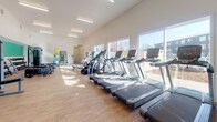 Located at 302 Morgantown Rd in Bowling Green, Kentucky, this fitness center offers a well-equipped, single-floor workout facility designed to support a full range of exercise routines. The space features soaring ceilings and large windows along one wall that flood the interior with abundant natural light, creating a bright and energizing environment.

The layout is thoughtfully organized to accommodate a variety of training styles. A row of treadmills lines the windowed wall, complemented by elliptical machines and stair climbers for a comprehensive cardio section. Strength training is well represented with a multi-station cable machine, a spin bike, and additional selectorized equipment. The free weights area includes a fully stocked dumbbell rack and multiple kettlebell sets of varying weights, along with flat benches and a functional training tire for dynamic workouts. Stability balls and medicine balls round out the functional fitness offerings.

The interior design balances clean white walls with a bold teal accent band that runs along the perimeter, giving the space a modern and motivating aesthetic. A large mural on the focal wall reads "The Spirit Makes the Master," reinforcing an encouraging atmosphere. The warm wood-toned flooring adds a welcoming feel underfoot. The facility is well-lit with linear overhead lighting, ensuring visibility throughout every section of the gym.