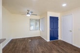 Located at 8021 9th St in Buena Park, California, this single-story residence offers a clean, functional layout with consistent hardwood-style flooring throughout. The spacious living area is filled with natural light streaming in through multiple windows and a sliding glass door that opens to an outdoor patio, where lush greenery provides a pleasant view. A ceiling fan and recessed lighting add to the room's practicality, while the textured ceiling and neutral walls create a warm, inviting atmosphere. A bold blue front door serves as a distinctive architectural accent and welcoming focal point upon entry. The kitchen is well-appointed with white cabinetry, granite-style countertops, and a full electric range with an overhead ventilation hood, providing ample storage and prep space. The bedrooms feature rich, dark hardwood-style flooring and windows that invite natural light. The bathrooms are finished with granite-top vanities, framed mirrors, and warm lighting fixtures. One full bathroom includes a tiled tub-shower combination, while a second bathroom functions as a half bath. Together, the thoughtful finishes and functional design make this Buena Park residence a well-rounded and comfortable space.