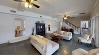 Located at 1421 Roper Mountain Rd in Greenville, SC, this single-floor space offers a thoughtfully designed interior that blends casual comfort with architectural character. The main living area is generously proportioned, anchored by striking slate tile flooring that extends throughout and contributes to the space's grounded, earthy aesthetic.

Vaulted, beamed ceilings rise overhead in portions of the space, adding a sense of volume and openness, while ceiling fans provide both function and a relaxed ambiance. Painted white brick walls lend a distinct architectural texture, complementing the neutral, warm tones of the interior palette. Crown molding and structural beam details add refined finishing touches throughout.

A wall of expansive French doors serves as a dramatic focal point, flooding the living area with natural light and offering sweeping views of an outdoor pool and patio. The seamless connection between indoor and outdoor living is a defining feature of this space. Additional French doors on an adjacent wall further enhance light flow and accessibility to the exterior.

A staircase with a classic wood railing adds visual interest and leads to an upper level. The space also includes built-in shelving niches, a dark wood display cabinet, and a wet bar or beverage station, rounding out its functional and inviting character.