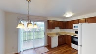 This two-floor residence offers a practical and comfortable layout designed for everyday living. The main level features a bright entryway with rich hardwood-style flooring that flows throughout the common areas, creating a warm and cohesive aesthetic. The living area is open and inviting, bathed in natural light from large windows, and includes a staircase leading to the upper floor.

The kitchen is well-appointed with rich wood cabinetry, light-toned countertops, and a full suite of appliances including a range, built-in microwave, dishwasher, and refrigerator. A sliding glass door connects the kitchen and dining area to a private balcony, offering pleasant outdoor views and an abundance of natural light. A pendant chandelier adds a decorative touch to the dining space.

The upper level hosts multiple bedrooms carpeted for comfort, each featuring baseboard heating and natural light from windows with blinds. The primary bedroom stands out with dual closets providing generous storage. Additional bedrooms offer similar functionality with ceiling-mounted light fixtures. The bathroom is clean and well-maintained, featuring a full tub and shower surround, a vanity with wood cabinetry, and hardwood-style flooring. Throughout the space, the neutral color palette and consistent finishes contribute to a tidy, move-in ready atmosphere.