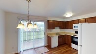 This two-floor residence offers a practical and comfortable layout designed for everyday living. The main level features a bright entryway with rich hardwood-style flooring that flows throughout the common areas, creating a warm and cohesive aesthetic. The living area is open and inviting, bathed in natural light from large windows, and includes a staircase leading to the upper floor.

The kitchen is well-appointed with rich wood cabinetry, light-toned countertops, and a full suite of appliances including a range, built-in microwave, dishwasher, and refrigerator. A sliding glass door connects the kitchen and dining area to a private balcony, offering pleasant outdoor views and an abundance of natural light. A pendant chandelier adds a decorative touch to the dining space.

The upper level hosts multiple bedrooms carpeted for comfort, each featuring baseboard heating and natural light from windows with blinds. The primary bedroom stands out with dual closets providing generous storage. Additional bedrooms offer similar functionality with ceiling-mounted light fixtures. The bathroom is clean and well-maintained, featuring a full tub and shower surround, a vanity with wood cabinetry, and hardwood-style flooring. Throughout the space, the neutral color palette and consistent finishes contribute to a tidy, move-in ready atmosphere.