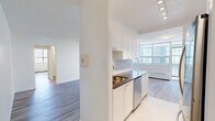 Located on the 9th floor at 1465 Lawrence Ave W in Toronto, this well-appointed 2-bedroom, 1-bathroom unit offers a clean, modern aesthetic throughout. Light wood laminate flooring flows consistently across the living spaces, complementing the crisp white walls and creating a bright, cohesive interior.

The open living room is generously proportioned, featuring large floor-to-ceiling windows that flood the space with natural light and offer views of the surrounding neighbourhood. A baseboard heating system runs along the window walls, ensuring comfort year-round. The kitchen is positioned adjacent to the living area and is fitted with white shaker-style cabinetry, dark countertops, a subway tile backsplash, and stainless steel appliances including a refrigerator, stove, microwave, and dishwasher. White tile flooring distinguishes the kitchen from the rest of the unit.

The primary bedroom is a well-sized retreat featuring large mirrored sliding closet doors and wood laminate flooring. The second bedroom also benefits from a large window with outdoor views and a baseboard heater. The bathroom is finished with classic white subway tile, a soaker tub, and a handheld shower fixture with chrome hardware, along with a window for natural ventilation. A hallway connects all rooms efficiently, completing this functional and stylish unit.