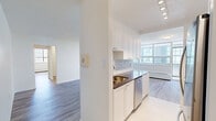 Located on the 9th floor at 1465 Lawrence Ave W in Toronto, this well-appointed 2-bedroom, 1-bathroom unit offers a clean, modern aesthetic throughout. Light wood laminate flooring flows consistently across the living spaces, complementing the crisp white walls and creating a bright, cohesive interior.

The open living room is generously proportioned, featuring large floor-to-ceiling windows that flood the space with natural light and offer views of the surrounding neighbourhood. A baseboard heating system runs along the window walls, ensuring comfort year-round. The kitchen is positioned adjacent to the living area and is fitted with white shaker-style cabinetry, dark countertops, a subway tile backsplash, and stainless steel appliances including a refrigerator, stove, microwave, and dishwasher. White tile flooring distinguishes the kitchen from the rest of the unit.

The primary bedroom is a well-sized retreat featuring large mirrored sliding closet doors and wood laminate flooring. The second bedroom also benefits from a large window with outdoor views and a baseboard heater. The bathroom is finished with classic white subway tile, a soaker tub, and a handheld shower fixture with chrome hardware, along with a window for natural ventilation. A hallway connects all rooms efficiently, completing this functional and stylish unit.