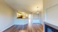 Located in Beaverton, Oregon, this one-bedroom, one-bathroom unit offers a well-designed layout across a single floor. The open living room is highlighted by soaring vaulted ceilings, rich hardwood-style flooring, and a tile-surround fireplace with a classic white mantel and built-in niche above. Sliding glass doors flood the space with natural light and open directly onto a private balcony overlooking lush greenery. The kitchen features white shaker cabinetry, grey quartz countertops, stainless steel appliances including a refrigerator and electric range, and a peninsula that connects seamlessly to the living area. A dedicated laundry area with a full-size washer and dryer is conveniently tucked nearby. The spacious bedroom is finished with plush carpet, vaulted ceilings, a large window, and a walk-in closet with built-in shelving. The bathroom includes a combination tub and shower with a curved curtain rod, a toilet, and hardwood-style flooring. A hallway with additional closet space completes the layout, providing practical storage throughout. The overall ambiance is clean, bright, and comfortable.