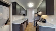This single-floor residence offers a thoughtfully designed layout with a cohesive blend of modern finishes and functional living spaces throughout. The galley-style kitchen is a standout feature, showcasing rich dark espresso cabinetry with brushed nickel hardware, light stone-look countertops, and a full suite of stainless steel appliances including an electric range, refrigerator, and dishwasher. Warm wood-look flooring runs through the kitchen and connects seamlessly to the main living areas, adding continuity and a clean aesthetic. The living room is generously proportioned, featuring neutral gray walls, a textured ceiling, and a full-width sliding glass door dressed with vertical blinds that invites natural light and provides direct outdoor access. An adjacent room features a large window with horizontal blinds and a soft blue accent wall, creating a bright and calming atmosphere. The bedrooms are finished with plush carpet, neutral tones, ample wall space, and windows that bring in natural light; one bedroom includes a closet with built-in storage. The bathroom is well-equipped with a dark wood vanity, stone-look countertop, large mirror, white tile surround, and accessibility-friendly grab bars. Textured ceilings are consistent throughout the space, adding a classic residential character to the overall design.