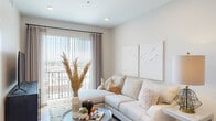 This contemporary single-floor residence offers a thoughtfully designed layout with a clean, modern aesthetic throughout. The living room serves as the heart of the space, featuring recessed lighting, warm wood-look flooring, and a sliding glass door that opens to a private balcony, flooding the room with natural light and providing outdoor views. Neutral tones and a calm, cohesive palette create an inviting and relaxed ambiance.

The open-concept kitchen is outfitted with crisp white upper cabinetry, light wood lower cabinets, and bright white quartz countertops that extend into a breakfast bar with seating. Stainless steel appliances — including a refrigerator, electric range, and over-the-range microwave — complement the clean, minimalist design, while a subway tile backsplash adds a subtle textural detail.

The bedroom is a serene retreat, featuring a window with outdoor views, soft natural light filtered through sheer curtains, and wood-look flooring that ties the space to the rest of the unit. The bathroom continues the modern design language with a dark charcoal vanity, white quartz countertop, a large framed mirror, and wood-look tile flooring, offering both style and function. Throughout, the space balances contemporary finishes with a warm, livable atmosphere.