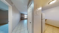 Located on Delmar Boulevard in St. Louis, Missouri, this single-floor unit offers a straightforward and functional layout finished consistently with light ceramic tile flooring throughout. An entry corridor leads into the main living area, which is a notably open space highlighted by a distinctive rounded structural column and a sliding window that allows natural light to fill the room. A wall-mounted HVAC unit provides climate control directly in the living space.

The kitchen is positioned adjacent to the living area and features a pass-through opening with a granite-patterned countertop that doubles as a casual breakfast bar. The kitchen is equipped with white cabinetry, a stainless steel sink with a modern pull-down faucet, and includes a dishwasher. Upper cabinets provide additional storage.

The bathroom is cleanly finished with white tile surrounding a full soaking tub and shower combination. It includes a toilet, a vanity with storage below, and tile flooring that complements the rest of the unit. The layout also includes a hallway with a panel box and access to a refrigerator, keeping utilities and appliances conveniently organized. Overall, the space presents a clean, neutral palette that offers a practical and versatile living environment.