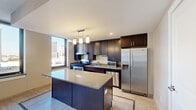 Located at 1212 Griswold St in the heart of downtown Detroit, this one-bedroom, one-bathroom unit offers a thoughtfully designed floor plan that maximizes its efficient footprint. The open-concept kitchen and living area serves as the centerpiece of the unit, featuring rich dark-wood cabinetry extending to the ceiling, a large center island with a light stone countertop, stainless steel appliances including a gas range, built-in microwave, dishwasher, and French door refrigerator, and a contemporary pendant light fixture overhead. Large windows in the kitchen frame striking views of the Detroit skyline, flooding the space with natural light. Light-toned tile flooring runs throughout the kitchen and living areas, complemented by mosaic tile border accents. The living area offers an open, versatile layout with warm neutral walls and tile flooring that transitions to plush carpet in the bedroom. The generously sized primary bedroom features two large windows with city views, soft carpeting, and a sliding double-door closet. In total, the unit includes four closets, providing exceptional storage. The bathroom is well-appointed with a soaking tub and shower combination, accessibility grab bars, stone-look tile flooring with a decorative mosaic border, and a vanity with dark countertops. A hallway connects the spaces efficiently, completing this functional urban residence.