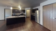 This three-bedroom, two-bathroom single-floor residence offers a practical and well-appointed layout designed for comfortable everyday living. Dark hardwood-style flooring flows throughout the main living areas, creating a cohesive and polished aesthetic, while neutral-toned walls provide a versatile backdrop throughout the space.

The kitchen serves as a central hub, featuring dark cabinetry, granite-style countertops, a central island with a built-in sink, stainless steel appliances including a gas range, microwave, and refrigerator, and a pantry with built-in shelving. Pendant lighting above the island adds a refined touch. The open layout connects the kitchen seamlessly to the spacious living area.

Both bathrooms are thoughtfully designed with accessibility in mind, equipped with grab bars, dark vanity cabinetry, and granite-style countertops. One bathroom includes a walk-in shower area with a handheld showerhead, while the other features a vanity with an open knee space and an adjacent walk-in closet with wire shelving.

The bedrooms are carpeted and include windows with blinds, baseboard heating, and wall-mounted air conditioning units. A dedicated laundry room houses a full-size washer and dryer, adding everyday convenience to this functional residence.