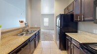 This single-floor residence offers a clean, neutral aesthetic throughout, with soft beige and gray tones creating a cohesive and welcoming atmosphere. The entryway opens into a spacious living area finished with plush wall-to-wall carpeting, allowing natural light to filter in through double windows fitted with white blinds. A pass-through counter separates the living space from the kitchen, enhancing the open feel of the layout. The kitchen is well-equipped, featuring rich dark espresso cabinetry, granite-style countertops, a double-basin sink, black appliances including a refrigerator, electric range, and built-in microwave, along with light tile flooring and track lighting overhead. A dedicated door provides convenient pantry or closet access. The bedroom is a comfortable, carpeted room with a ceiling fan, a bright window with blinds for natural light and privacy, and ample wall space. The full bathroom is neatly appointed with a dark wood vanity, granite-style countertop, a large mirror, tile flooring, and a full tub and shower combination. Throughout the residence, clean white baseboards, recessed vents, and consistent finishes contribute to a tidy, move-in-ready presentation. The overall layout is practical and efficiently designed for comfortable everyday living.