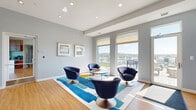 Located at 1600 Pennsylvania Ave SE in Washington, DC, this well-appointed amenity space offers a thoughtfully designed layout across a single floor. The living room is a bright, contemporary gathering area featuring warm hardwood-style flooring, recessed lighting, and large floor-to-ceiling windows that flood the space with natural light while framing sweeping views of the surrounding landscape and waterway. Modern swivel lounge chairs and sectional seating are arranged atop bold area rugs, creating an inviting and functional atmosphere. A wall-mounted television and media console add a practical, connected touch.

The hallway serves as a memorable transition space, highlighted by a striking large-scale floral mural that brings vibrant color and artistic energy to the interior. Continuity in flooring ties the two areas together seamlessly.

Beyond the interior, a generously sized rooftop terrace elevates the experience with teak-style deck tiles, turf lounging areas, and multiple outdoor seating arrangements. Protected by glass-panel railings, the terrace offers unobstructed panoramic views of the Anacostia River, surrounding greenery, and the Washington, DC skyline — making it an exceptional outdoor retreat. A charming brick pavilion with a slate roof anchors one section of the terrace, adding architectural character to the outdoor space.