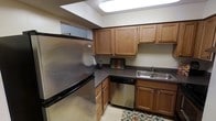This single-floor residence offers a thoughtfully designed living environment with a focus on functionality and comfort. The kitchen stands out as a highlight of the space, featuring warm honey-toned wood cabinetry that extends to both upper and lower sections, providing ample storage throughout. Stainless steel appliances, including a full-size refrigerator and a built-in dishwasher, lend a clean, modern feel to the kitchen. The countertops are finished in a dark speckled laminate, offering a practical and durable workspace. A double stainless steel sink is positioned beneath a dedicated area with straightforward access, while a skylight above the kitchen fills the space with natural light, brightening the room and enhancing the overall ambiance. The kitchen layout is efficiently arranged in an L-shape, making the most of the available space and allowing for ease of movement during meal preparation. The light tile flooring adds a neutral, clean foundation that complements the warm wood tones throughout. Overall, the space presents a welcoming and practical atmosphere suited to comfortable everyday living.