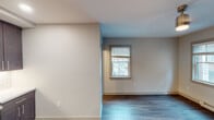 This thoughtfully designed single-floor space combines modern finishes with functional living. The kitchen stands out as a centerpiece, featuring rich dark-stained shaker-style cabinetry that extends to the ceiling for maximum storage, light stone countertops, a classic white subway tile backsplash, and a full suite of stainless steel appliances including a dishwasher, range, and over-the-range microwave. The durable hardwood-style flooring flows consistently throughout the space, tying each room together seamlessly.

The main living area is bright and open, benefiting from multiple windows fitted with blinds that allow for natural light while maintaining privacy. A wall-mounted mini-split HVAC unit ensures year-round climate comfort, complemented by baseboard heating. A ceiling-mounted light fixture adds a subtle industrial touch to the room.

The bedroom offers generous proportions with two windows providing ample natural light and views to the outdoors. A substantial built-in closet with bifold dark wood doors features a multi-tier wire shelving system for organized storage.

The bathroom is elegantly finished with large-format marble-look tile lining the tub and shower surround, accented by a vertical mosaic tile detail. A soaking tub, pedestal-style vanity, and toilet complete this clean, bright space.