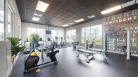 Located at 7065 Banyan Leaf Dr in West Palm Beach, Florida, this single-floor fitness center is a comprehensively outfitted exercise facility designed to support a wide range of workout routines. The space features a dark tiled drop ceiling with recessed panel lighting that provides consistent, even illumination throughout. Durable rubber flooring covers the entire area, offering both safety and comfort underfoot.

Large windows line multiple walls of the facility, flooding the interior with natural light and offering views of the surrounding outdoor amenities, including a pool area and neighboring buildings. This connection to the outdoors enhances the overall atmosphere of the space.

The fitness center is divided into functional zones. A dedicated cardio area houses multiple treadmills, elliptical machines, and stationary bikes, positioned to take advantage of the exterior views. A strength training zone features a full dumbbell rack with a wide weight range, weight benches, cable machines, and resistance equipment. Stability balls and medicine balls are also available for functional training.

Full-length mirrors along one wall visually expand the space, while wall-mounted televisions provide entertainment. Bold motivational typography adorns the walls, reinforcing an energetic and encouraging atmosphere. Glass doors provide direct outdoor access, contributing to a bright, open, and welcoming environment.