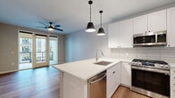This single-floor residence showcases a clean, contemporary design with warm hardwood-style flooring and soft neutral tones carried throughout every room. The open-concept kitchen and living area serves as the heart of the space, anchored by a central island with a stainless steel undermount sink, integrated dishwasher, and crisp white quartz countertops. Sleek white cabinetry lines the walls above a textured subway tile backsplash, complemented by a full suite of stainless steel appliances including a gas range, microwave, and refrigerator. Two matte black pendant lights hang above the island, while a ceiling fan provides additional comfort in the adjoining living area. Glass doors open directly to a private balcony, allowing natural light to fill the space.

The bedrooms are generously proportioned, each featuring large windows with outdoor views and ample closet storage with built-in shelving. The bathroom is finished with a tiled tub-and-shower combination, brushed nickel fixtures, and a clean white vanity. A well-lit hallway connects all rooms and leads to a dedicated in-unit laundry area, adding everyday convenience to this thoughtfully designed residence.
