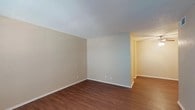 This single-floor space offers a practical and well-organized layout designed for comfortable everyday living. The main living areas feature warm, wood-look laminate flooring that runs throughout, complementing the neutral beige walls and white baseboards that give the space a clean, cohesive aesthetic. Textured ceilings are present throughout, adding a subtle dimensional quality to each room.

The open living area is generously proportioned, providing ample room for a variety of furniture arrangements. A dedicated entry door opens directly into the living space, which is served by ceiling-mounted HVAC vents for year-round climate control.

The galley-style kitchen is efficiently designed, featuring white raised-panel cabinetry on both sides, dark granite-style countertops, wood-look flooring, and white appliances including a coil-burner range, over-the-range microwave, and dishwasher. A stainless steel sink completes the functional workspace.

The bedrooms are carpeted in a neutral tone and each include a ceiling fan with light fixture. One bedroom features a window with horizontal blinds, allowing natural light to filter in while maintaining privacy.

The bathroom is well-appointed with a white vanity, dark countertop, a tiled shower-tub combination, and wood-look flooring, maintaining the consistent design language found throughout the space.