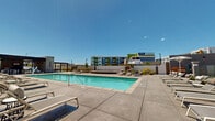 Located at 3811 Commerce Way in Sacramento, CA, this thoughtfully designed outdoor amenity space offers a resort-inspired experience tailored for community living. At the heart of the space is a generously sized swimming pool with crystal-clear water, complemented by an adjacent spa, both surrounded by a broad concrete sun deck lined with lounge chairs and shaded umbrella stations for relaxed outdoor enjoyment under the California sun.

A covered outdoor kitchen and lounge area anchors one end of the property, featuring a striking natural stone accent wall, a large center island with a dark countertop and integrated sink, pendant lighting, and a flat-screen display. The open-air design of this space allows seamless views of the pool deck, making it well-suited for gatherings and social events.

Adjacent to the kitchen pavilion, a dedicated bocce ball court is framed by timber borders and set against a backdrop of manicured green lawn and low-water landscaping. A pergola-covered seating area with bench seating provides a comfortable spot to relax nearby.

The overall design blends modern contemporary architecture — characterized by bold red and neutral facades with large windows and balconies — with warm natural stone elements, lush plantings, and open sightlines. The space is fully enclosed by a perimeter wall and iron fencing, ensuring privacy while maintaining an open, airy atmosphere throughout.