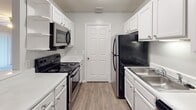 Located at 100 Crown Point Cir NW in Concord, North Carolina, this single-floor residence offers a well-organized layout with a practical and comfortable design throughout. The galley-style kitchen is outfitted with white shaker cabinetry, white countertops, a stainless steel sink, and black appliances including an electric range, over-the-range microwave, and refrigerator. Wood-look flooring runs through the kitchen, adding warmth and durability to the space.

The open living and dining area is generously sized, featuring neutral carpet, a textured ceiling, and a ceiling fan. A pass-through countertop connects the kitchen to the main living space, promoting an open and airy feel. Natural light filters in through windows that frame views of the surrounding greenery.

The bedrooms are carpeted and well-proportioned, each equipped with a ceiling fan and light kit, a window with outdoor views, and access to closet space. The rooms are finished with neutral-toned walls and clean white trim throughout.

Two full bathrooms serve the residence, each featuring a shower-tub combination with chrome fixtures, a toilet, and wood-look flooring. One bathroom also includes a white vanity with an integrated sink and a large mirror. Panel-style doors are used consistently throughout the home, contributing to a cohesive interior aesthetic.