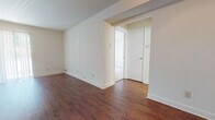 This single-floor residence offers a well-organized layout with distinct living areas connected by a practical, open flow. The main living spaces are finished with rich, dark hardwood flooring that extends throughout the primary rooms, lending warmth and visual continuity to the interior. A ceiling fan with a light fixture is installed overhead, providing both airflow and ambient lighting. Neutral, light-toned walls throughout the space create a clean and versatile backdrop.

Large vertical-blind-covered windows and a sliding glass door allow generous natural light to filter into the living areas, brightening the interior and offering outdoor access. The spacious layout is visible from multiple vantage points, conveying a comfortable sense of openness.

The bedroom is finished with wall-to-wall carpet in a neutral tone and features a large window with vertical blinds, providing additional natural light and a quiet, restful atmosphere.

The kitchen is equipped with light wood cabinetry, light-toned countertops, and a black Whirlpool electric coil range with oven, offering functional cooking space.

The bathroom features tile flooring in warm earth tones, a white vanity with under-sink storage, a wall mirror, a tub-shower combination, and bright overhead lighting, presenting a clean and efficient design.