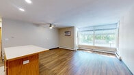 Located at 405 Tenth Ave N in South Saint Paul, MN, this single-floor, one-bedroom, one-bathroom unit offers a practical and comfortable layout. The open-concept kitchen and living area serves as the heart of the home, with warm hardwood-style flooring flowing throughout. The kitchen is well-equipped with oak cabinetry, a stainless steel refrigerator, a gas range, a double sink, and a central island with a white countertop that provides additional workspace and casual dining. Recessed lighting and a ceiling fan enhance the functionality and comfort of the shared living space. The living room is bright and airy, featuring large windows that allow generous natural light to fill the room, with a baseboard heating system ensuring warmth year-round. The bedroom is a comfortable, well-proportioned space with its own window for natural light, a wall-mounted air conditioning unit, a ceiling fan, and a sliding-door closet with ample storage. The bathroom features classic mosaic tile flooring in white with colorful accents, a white walk-in shower with grab bars, a pedestal-style sink with a vanity cabinet, and a mirror. Throughout the unit, warm wood-toned doors and trim add a cohesive, inviting character to the overall design.