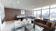 This stylish lounge space in Dallas offers an impressive blend of urban sophistication and contemporary design. The single-floor layout is anchored by dramatic floor-to-ceiling glass windows that frame sweeping panoramic views of the Dallas skyline, flooding the interior with abundant natural light throughout the day.

Exposed brick walls serve as a defining architectural element, adding warmth and texture that contrasts beautifully with the clean white ceilings and smooth flooring. The space is divided into distinct seating areas, each thoughtfully arranged for comfort and conversation. A lounge area features crisp white armchairs and a glass-topped coffee table set atop a teal area rug, while a separate seating zone offers a plush brown sofa with coordinating accent pieces.

A media area is built into a rich crimson accent wall, housing a large flat-screen television above dark wood cabinetry and flanked by large-scale abstract artwork on the adjacent brick wall. A communal dining or gathering table with upholstered bench seating and woven ottoman stools provides additional functionality, adorned with sculptural white ceramic vases. The overall ambiance is polished and modern, making it an inviting and versatile space well-suited for both relaxation and socializing.