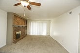 This single-story space offers a practical and comfortable layout across several rooms. The living area serves as the heart of the home, highlighted by a full brick fireplace with a wood mantle and raised brick hearth, adding warmth and character. A ceiling fan with overhead lighting keeps the space comfortable, while large vertical blinds along a wide sliding door allow natural light to filter through. The carpet throughout the living and bedroom areas provides a soft, neutral foundation.

The kitchen sits adjacent to the living area in an open-pass configuration, featuring dark wood cabinetry, white laminate countertops, a gas range with overhead ventilation, and a stainless steel sink. Cabinet storage is available both above and below the counters.

The bedrooms are carpeted and bright, with white walls, textured ceilings, and windows fitted with blinds. At least one bedroom includes bifold closet doors offering generous storage space.

Two bathrooms serve the unit. One features a glass-enclosed walk-in shower, a white vanity with under-sink storage, and tile flooring. The second bathroom offers a full soaking tub with a shower, a matching white vanity, and the same tile flooring, providing functional versatility for residents.