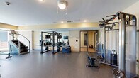 Located at 1462 80th St E in Inver Grove Heights, MN, this fitness center offers a comprehensive, single-floor layout designed to support a wide range of workout routines. The main exercise room is generously proportioned, featuring durable rubber flooring ideal for high-traffic athletic use and warm, neutral-toned walls that create an energizing yet comfortable environment. Natural light filters in through large windows along one wall, offering pleasant outdoor views and a bright, open atmosphere enhanced by recessed lighting and ceiling fans overhead.

The space is well-stocked with a diverse selection of equipment, including treadmills, stair climbers, stationary bikes, a rowing machine, and an elliptical trainer for cardiovascular workouts. Strength training is well-represented with a power rack, cable resistance systems, a weight bench, and a full dumbbell rack spanning a wide range of weights. An accent brick wall adds a distinctive architectural touch, lending character to the otherwise modern, functional interior.

Adjacent to the main gym floor is a separate exercise room featuring light hardwood-style flooring, mirrored walls, and a wall-mounted TV — ideal for stretching, yoga, or guided workouts. Together, these spaces form a thorough and thoughtfully arranged fitness facility suited for a variety of fitness levels and training styles.