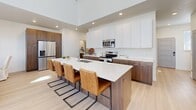 Located in South Jordan, Utah, this thoughtfully designed two-story home offers a modern aesthetic with clean lines and high-end finishes throughout. The main level features a striking open-concept kitchen and living area anchored by soaring ceilings and abundant natural light streaming through large windows. The chef's kitchen is a standout, boasting a generous island with bar seating, two-tone cabinetry pairing rich walnut lower cabinets with crisp white uppers, quartz countertops, and stainless steel appliances. Light wood flooring runs throughout the main living areas, enhancing the bright, airy atmosphere. A dedicated hallway leads past multiple closets and well-appointed bathrooms featuring warm walnut vanities and white quartz surfaces. The lower level hosts a spacious family room with plush carpet, a comfortable bedroom with a horizontal window, a dedicated office with carpet flooring and natural light, and a laundry room. Five bathrooms are distributed across both floors, offering convenience and privacy. The home also includes an attached garage and an outdoor patio. With nine closets providing exceptional storage, this residence combines practical functionality with modern, cohesive design from top to bottom.