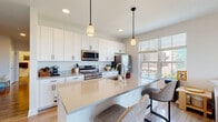 Located at 140 E Monument Ave in Dayton, Ohio, this contemporary single-floor residence offers a thoughtfully designed layout with modern finishes throughout. The open-concept kitchen is a standout feature, showcasing crisp white cabinetry extending to the ceiling, stainless steel appliances including a refrigerator, range, and over-the-range microwave, and a generous island with light quartz countertops and seating for casual dining. Pendant lighting and natural light from large windows overlooking the cityscape complete the space. Hardwood-style flooring flows through the kitchen and hallways, connecting the living spaces seamlessly. The bright and airy living room is anchored by floor-to-ceiling sliding glass doors that open to a private balcony, offering expansive views of the surrounding landscape and city skyline. The bedrooms are comfortably proportioned, featuring plush carpet, ample natural light from well-placed windows, and closet access. The bathroom is clean and functional, with a shower-tub combination and neutral finishes. A well-lit hallway with light wood flooring connects all rooms, lending the home a cohesive and modern feel. The overall ambiance is calm and contemporary, with a neutral palette that enhances the sense of openness throughout.
