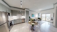 This contemporary single-floor residence combines modern design with functional living spaces throughout. The expansive main living area immediately impresses with its large format black-framed sliding glass doors that span nearly the full width of one wall, flooding the space with natural light. Dark hardwood flooring, crown molding with gray accents, recessed lighting, and a ceiling fan complete the polished aesthetic of this open-plan area.

The kitchen is outfitted with high-gloss gray cabinetry extending to the ceiling, white quartz countertops, a marble-inspired tile backsplash, and a full suite of stainless steel appliances including a French door refrigerator, electric range with over-the-range microwave, and ample under-cabinet lighting.

The bedrooms are generously sized, each featuring dark hardwood floors, ceiling fans, and access to dedicated closets with built-in shelving systems. One room includes a large walk-in closet with dual hanging rods and a central shelving unit, providing extensive storage capacity.

The primary bathroom is finished with a dual-sink vanity topped in white countertops, a large wall mirror, elegant vanity lighting, and a deep soaking tub, all set against crisp white walls and continued dark hardwood flooring. The overall design palette of whites and grays creates a clean, cohesive, and modern atmosphere throughout.