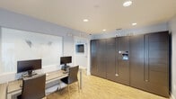 Located at 1834 Jackson Bluff Rd in Tallahassee, Florida, this single-story amenity space is designed to support productivity and convenience for its users. The interior is finished with light hardwood-style flooring, soft blue-gray walls, and recessed lighting throughout, creating a clean and professional atmosphere.

The business center area features a workstation desk with dual monitors, providing a functional workspace for everyday computing needs. Adjacent to it stands a large bank of Package Concierge smart lockers, offering a secure and automated solution for package retrieval.

The space also includes a dedicated conference room furnished with a spacious wood-grain conference table and ergonomic mesh chairs, accommodating multiple attendees comfortably. A bold teal geometric accent wall serves as a striking visual focal point in this room, complemented by white window blinds that allow for natural light control. A pass-through window connects to a secondary meeting or breakout room, which features a warm wood dining-style table with leather chairs, ideal for smaller group discussions.

The floorplan, as visible in the dollhouse view, reveals a well-organized layout with clearly defined zones for collaboration and package management. The overall design balances modern aesthetics with practical functionality, making this a versatile and well-appointed communal facility.