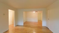 This single-floor space presents a clean and functional layout defined by warm hardwood flooring that runs throughout, creating a sense of continuity and cohesion across the interior. The living areas are openly connected through a wide architectural passageway, allowing for a natural flow between spaces. This open-concept design enhances the overall sense of roominess and flexibility in how the space can be arranged and utilized.

The interior features neutral white walls that provide a bright, airy backdrop well-suited to a variety of décor styles. A ceiling fan is installed in the adjoining room, contributing both to comfort and to the practical character of the space. White baseboards and trim add a crisp finishing detail throughout.

The hardwood floors, with their warm honey tones, are a standout feature, lending both durability and timeless appeal. The overall ambiance is understated and versatile — an inviting blank canvas ready to be personalized. The open passage between rooms encourages an easy, interconnected living experience, making the space feel expansive and well-proportioned for everyday living.