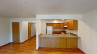 This single-floor unit is thoughtfully laid out to maximize functionality across its living spaces. The kitchen serves as a central highlight, featuring warm honey-toned oak cabinetry extending to the ceiling for ample storage, granite-look countertops, and white appliances including a Whirlpool electric range with an overhead ventilation hood and a full-size refrigerator. A peninsula with matching countertop and oak paneling separates the kitchen from the adjacent living area, providing a practical breakfast bar while maintaining an open, connected feel. Recessed lighting illuminates the kitchen workspace effectively.

The living areas are finished with light-toned hardwood flooring, which extends through the main living space and into at least one bedroom. A sliding glass door fitted with vertical blinds allows natural light to flow into the living room and provides outdoor access. A secondary bedroom features carpeting and a window overlooking the exterior. The bathroom is equipped with a full tub-shower combination in white, complemented by tile flooring. Throughout the unit, textured ceilings, neutral wall tones, and consistent wood-toned trim elements create a cohesive and practical interior aesthetic.