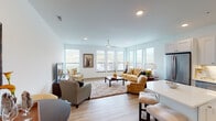 Located at 123 Fourth Ave in Dayton, Kentucky, this single-floor residence offers a thoughtfully designed open-concept layout with clean, modern finishes throughout. Light hardwood flooring flows seamlessly across every room, complementing the crisp white walls and creating a bright, cohesive aesthetic.

The expansive living area is a standout feature, anchored by a bank of large windows that frame sweeping outdoor views of the surrounding landscape and skyline. A ceiling fan overhead and recessed lighting ensure year-round comfort, while the generous floor plan easily accommodates multiple seating arrangements.

The kitchen is well-appointed with white shaker-style cabinetry, quartz countertops, a classic subway tile backsplash, and a full suite of stainless steel appliances. A central island with seating provides an ideal space for casual dining or entertaining, and a separate dining area offers additional flexibility.

The bedroom is a serene retreat, featuring a spacious closet with built-in shelving, a ceiling fan, and a window that invites natural light. The bathroom includes a clean white vanity with ample cabinet storage, a wide mirror, and polished hardware.

Throughout the residence, the design emphasizes natural light, open sightlines, and functional elegance, making this a well-rounded and inviting living space.