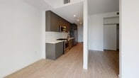 Located at 222 W Sixth St in San Pedro, Los Angeles, this single-floor unit offers a thoughtfully designed layout with modern finishes and a clean, minimalist aesthetic. Light wood-style flooring runs throughout the space, complementing the crisp white walls and creating a bright, cohesive atmosphere.

The kitchen is a standout feature, outfitted with dark charcoal cabinetry that extends to the ceiling for ample storage, white subway tile backsplash, light countertops, and a full suite of stainless steel appliances including a gas range, over-the-range microwave, dishwasher, and refrigerator. Recessed lighting adds a polished touch to this well-appointed cooking space.

A dedicated hallway provides access to an in-unit stacked washer and dryer tucked behind louvered closet doors — a highly functional feature that adds day-to-day convenience. The living area is generously proportioned, filled with natural light from a large picture window that frames views of the surrounding building complex and brings warmth into the room.

The bedroom offers a quiet, open space with light-toned flooring and clean walls, providing a neutral canvas for personalization. The bathroom is finished with tile flooring, a full soaking tub with shower and curved rod, a wall-mounted mirror, and safety grab bar, balancing practicality with comfort.
