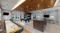 Located at 2599 Evans Rd in Morrisville, NC, this single-floor community amenity space is thoughtfully designed to encourage gathering, recreation, and relaxation. The open-concept layout flows seamlessly between distinct zones, all unified by warm hardwood-style flooring and a striking slatted wood ceiling with recessed and ambient lighting that adds depth and warmth throughout.

The main game and lounge area is a standout, featuring a pool table, shuffleboard, and a large dark island with bar-height seating illuminated by sculptural pendant fixtures. Generous sectional sofas, layered rugs, and accent chairs create an inviting lounge zone anchored by a wall-mounted flat-screen TV. Large windows along multiple walls flood the space with natural light and offer views of the surrounding community.

A dedicated kitchen area serves the space with practical elegance. Gray shaker-style cabinetry pairs with light stone countertops, while a bold Arabesque-patterned tile backsplash in teal and white adds a decorative focal point. Open floating shelves in dark wood display serveware and accessories, completing the functional yet stylish design. The overall ambiance is modern and sophisticated, balancing comfort with a refined, upscale aesthetic ideal for community events and everyday leisure.