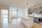 Located in Charlotte's vibrant Dilworth neighborhood, this contemporary 2-bedroom, 3-bathroom residence offers a thoughtfully designed open-concept layout with modern finishes throughout. Light wood-tone flooring flows seamlessly across the entire unit, creating a cohesive and airy feel.

The kitchen is a standout centerpiece, featuring gray shaker-style cabinetry with matte black hardware, a white quartz waterfall island, subway tile backsplash, stainless steel appliances, and sleek pendant lighting. The kitchen opens directly into the living area, which is anchored by a ceiling fan and access to a private balcony, filling the space with natural light.

Both bedrooms are well-proportioned and bright, each benefiting from large windows with outdoor views and ceiling fans. The primary bedroom includes a dedicated closet and an en-suite bathroom with dual vanity sinks, gray cabinetry, a large framed mirror, and a glass-enclosed walk-in shower finished in marble-style tile with a built-in bench. Two additional closets provide ample storage throughout the unit.

The clean white walls, recessed lighting, and consistent use of quality materials lend a polished, move-in-ready aesthetic that suits both everyday living and entertaining.