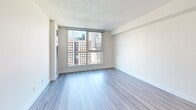 Located on the 18th floor at 235 Bloor Street East in Toronto's Bloor-Yorkville neighbourhood, this studio unit offers a compact yet efficiently designed single-floor layout. The open-concept living and kitchen area forms the heart of the space, finished with light wood-tone laminate flooring throughout. A large floor-to-ceiling window floods the living area with natural light while framing impressive views of Toronto's downtown skyline — a standout feature of the unit.

The kitchen is modern and well-appointed, featuring white high-gloss cabinetry extending to the ceiling, white quartz countertops, stainless steel appliances including an electric range, built-in microwave, and dishwasher, as well as an in-unit washer. A peninsula counter provides additional workspace and visual separation from the living area.

The bathroom is clean and contemporary, finished with light tile flooring and white fixtures, including a single-sink vanity with under-cabinet storage, a framed mirror, and a full bathtub with shower. A hallway connects the main living area to the bathroom, providing a defined transition within the space.

Neutral white walls and recessed lighting throughout contribute to a bright, modern ambiance suited to efficient urban living.