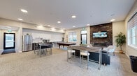 Located at 5000 Green Jewel Blvd in Regina, Saskatchewan, this single-floor clubhouse offers a thoughtfully designed amenity space for residents. The open-concept main area is bright and welcoming, featuring recessed pot lighting, neutral-toned carpet tiles, and large windows that invite natural light and outdoor views. A striking stacked-stone accent wall anchors the lounge area, showcasing a linear fireplace and a wall-mounted television — an ideal setting for relaxed gatherings. Comfortable seating, including leather sofas and accent chairs, surrounds a central coffee table, complemented by lush indoor plants that add warmth throughout.

The social and entertainment area includes a full-sized pool table and bar-height tables with stools, providing versatile space for casual socializing. The kitchenette is well-equipped with stainless steel appliances — including a full-sized refrigerator, dishwasher, and microwave — along with crisp white upper cabinetry, dark lower cabinetry, and a clean tile backsplash.

Two private meeting rooms offer quieter settings for focused work or small group discussions, each furnished with a round wooden table, upholstered chairs, and decorative artwork. A comfortable waiting area with cream-toned lounge chairs completes this well-rounded community space.