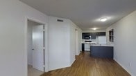 This single-floor residential space offers a practical and well-designed layout that blends comfort with functionality. The open-concept floor plan connects the living area to the kitchen, creating a seamless flow throughout the main living space. Hardwood-style flooring runs through the main areas, lending a warm and cohesive aesthetic, while carpeting is visible in adjacent rooms, adding a softer touch to private spaces. The kitchen is a standout feature, equipped with dark cabinetry that contrasts cleanly against white appliances, including a range, microwave, and refrigerator. A dark-finished kitchen island provides additional prep and storage space, anchoring the kitchen within the open layout. A stainless steel sink sits beneath overhead cabinetry, maximizing utility. The walls throughout are painted in a crisp, neutral white, contributing to a bright and airy atmosphere. Ceiling-mounted light fixtures provide consistent illumination, while HVAC vents are integrated discreetly into the ceiling. A textured ceiling adds subtle architectural character. Doorways lead to additional rooms, offering defined private spaces while maintaining an overall sense of openness. The unit presents a clean, move-in-ready environment suited for everyday living.