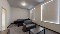 Located at 101 Erie Street in Cheney, WA, Unit 129 is a single-floor residential unit designed to accommodate comfortable shared living. The layout, as revealed by the floor plan, includes two separate bedroom areas, a kitchen, and bathroom facilities, all arranged for functional everyday use.

Each bedroom is carpeted and features lofted or raised bed frames with built-in drawer storage underneath, a loveseat-style sofa, a coffee table, and a nightstand — providing a combined sleeping and lounging area within a single room. Large windows dressed with roller shades allow natural light to fill the spaces while maintaining privacy. Each room also includes a walk-in or open closet with wire shelving for storage.

The kitchen is well-appointed with dark espresso-toned cabinetry, white quartz-style countertops, and a full suite of black appliances including an electric range, over-the-range microwave, and dishwasher. The flooring in the kitchen transitions to a light-toned hard surface, contrasting with the carpeted living areas.

The bathrooms feature full-sized soaking tubs with tub-shower combos and chrome fixtures set against clean white surrounds, complemented by neutral tile flooring. The unit's overall aesthetic is clean and neutral, with textured walls and efficient use of space throughout.
