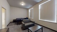Located at 101 Erie Street in Cheney, WA, Unit 129 is a single-floor residential unit designed to accommodate comfortable shared living. The layout, as revealed by the floor plan, includes two separate bedroom areas, a kitchen, and bathroom facilities, all arranged for functional everyday use.

Each bedroom is carpeted and features lofted or raised bed frames with built-in drawer storage underneath, a loveseat-style sofa, a coffee table, and a nightstand — providing a combined sleeping and lounging area within a single room. Large windows dressed with roller shades allow natural light to fill the spaces while maintaining privacy. Each room also includes a walk-in or open closet with wire shelving for storage.

The kitchen is well-appointed with dark espresso-toned cabinetry, white quartz-style countertops, and a full suite of black appliances including an electric range, over-the-range microwave, and dishwasher. The flooring in the kitchen transitions to a light-toned hard surface, contrasting with the carpeted living areas.

The bathrooms feature full-sized soaking tubs with tub-shower combos and chrome fixtures set against clean white surrounds, complemented by neutral tile flooring. The unit's overall aesthetic is clean and neutral, with textured walls and efficient use of space throughout.