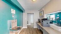 Located at 1717 Aberdeen Rd in Towson, Maryland, this compact single-room office is a efficiently designed workspace that makes excellent use of its footprint. The room features light wood-tone luxury vinyl plank flooring throughout, contributing to a clean and modern aesthetic.

A continuous built-in workstation with gray cabinetry runs along one wall, providing ample desk surface to accommodate multiple computer workstations and a printer — making it well-suited for administrative or shared office use. A bright, grid-paned window allows natural light to fill the space, enhancing the open feel of the room.

A bold teal accent wall adds a pop of color and visual interest, contrasting with the neutral gray and white tones that dominate the rest of the room. Framed artwork further personalizes the environment. A built-in water fountain and bottle-filling station is mounted along the teal wall, offering a practical and modern amenity.

The office connects through a doorway to an adjacent hallway, suggesting its role as part of a larger facility. A thermostat and HVAC vent are visible, ensuring climate comfort. The overall ambiance is functional yet inviting, with thoughtful design details that create a productive and welcoming workspace.