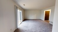 Located at 5004 S Webster St in Kokomo, Indiana, Unit C is a single-floor residence that offers a practical and comfortable layout. The main living area is generously sized, featuring neutral-toned carpet and crisp white walls that create a clean, open atmosphere. A full-width sliding glass door floods the space with natural light and provides direct access to a wooden deck, which overlooks a pleasant outdoor setting with mature trees — a welcoming extension of the living space.

The kitchen is equipped with warm oak cabinetry, golden-toned countertops, and a white electric range with an overhead ventilation hood, providing a functional cooking environment with ample storage. The bathroom features a full-size tub and shower combination with built-in shelving niches and chrome fixtures, finished in a clean, neutral palette.

The bedrooms are carpeted and well-proportioned, each offering a calm, neutral backdrop. One bedroom benefits from a large window with views of the surrounding neighborhood, allowing for excellent natural light throughout the day. The textured ceilings and consistent neutral tones throughout the unit contribute to a cohesive and move-in-ready aesthetic. The overall layout, as seen from the dollhouse view, is efficient and logically organized for everyday living.